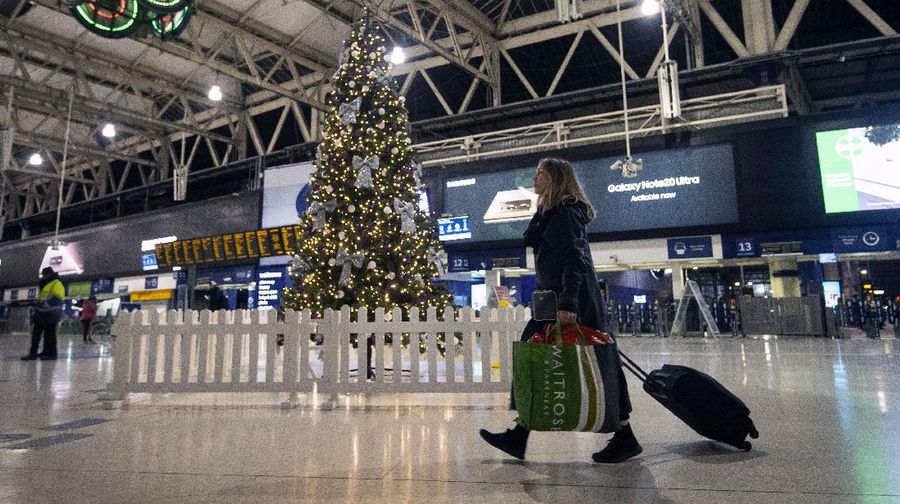 Seorang wanita menarik koper melewati pohon Natal di terminal Stasiun Waterloo di pusat kota London, Minggu (20/12/2020)