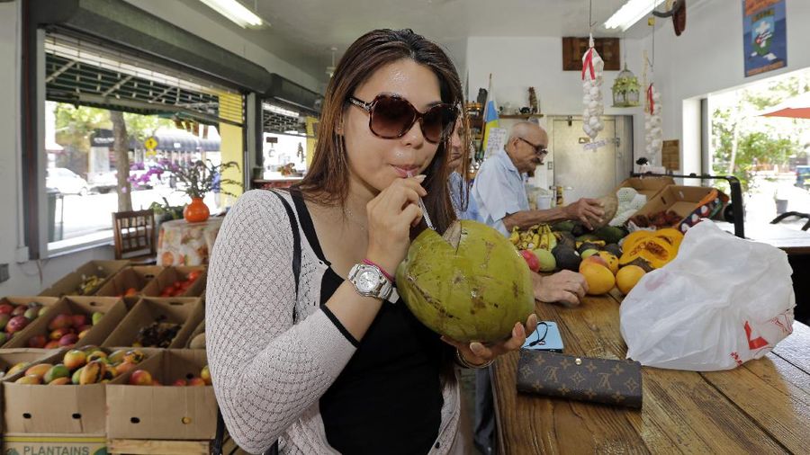 In this photo taken Tuesday, June 9, 2015, Lillian Nguyen, of New York, sips coconut water at a fruit store in the Little Havana area of Miami. (AP Photo/Alan Diaz)