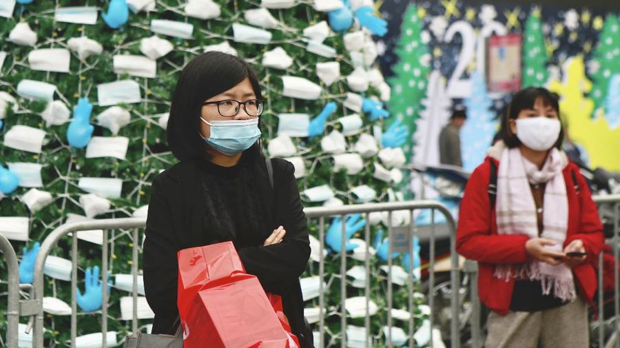 A masked security guard stands watch in front of a coronavirus-themed Christmas tree decorated with masks and rubber gloves in Hanoi, Vietnam, Thursday, Dec. 24, 2020. (AP Photo/Hau Dinh)