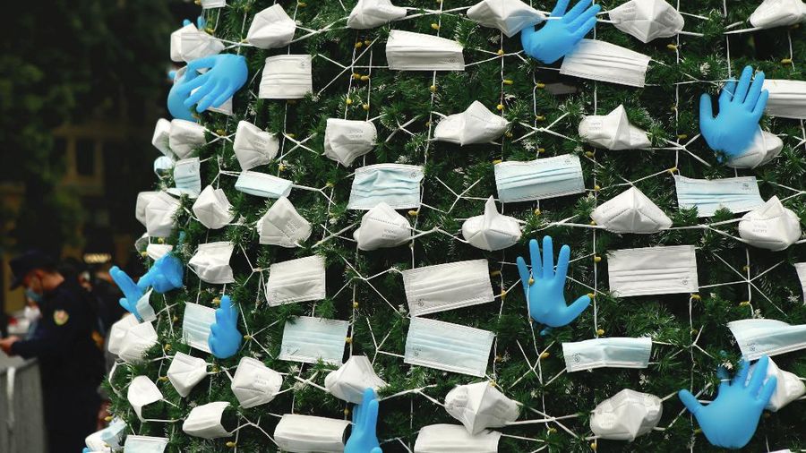 A masked security guard stands watch in front of a coronavirus-themed Christmas tree decorated with masks and rubber gloves in Hanoi, Vietnam, Thursday, Dec. 24, 2020. (AP Photo/Hau Dinh)