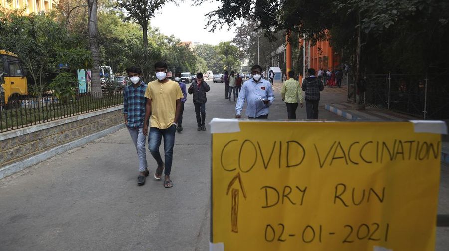 People walk past a poster placed outside a Government Hospital during a COVID-19 vaccine delivery system trial in Hyderabad, India, Saturday, Jan. 2, 2021. India tested its COVID-19 vaccine delivery system with a nationwide trial on Saturday as it prepares to roll-out an inoculation program to stem the coronavirus pandemic. Saturday's exercise included necessary data entry into an online platform for monitoring vaccine delivery, along with testing of cold storage and transportation arrangements for the vaccine, the health ministry had said.(AP Photo/Mahesh Kumar A.)