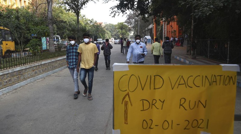 People walk past a poster placed outside a Government Hospital during a COVID-19 vaccine delivery system trial in Hyderabad, India, Saturday, Jan. 2, 2021. India tested its COVID-19 vaccine delivery system with a nationwide trial on Saturday as it prepares to roll-out an inoculation program to stem the coronavirus pandemic. Saturday's exercise included necessary data entry into an online platform for monitoring vaccine delivery, along with testing of cold storage and transportation arrangements for the vaccine, the health ministry had said.(AP Photo/Mahesh Kumar A.)