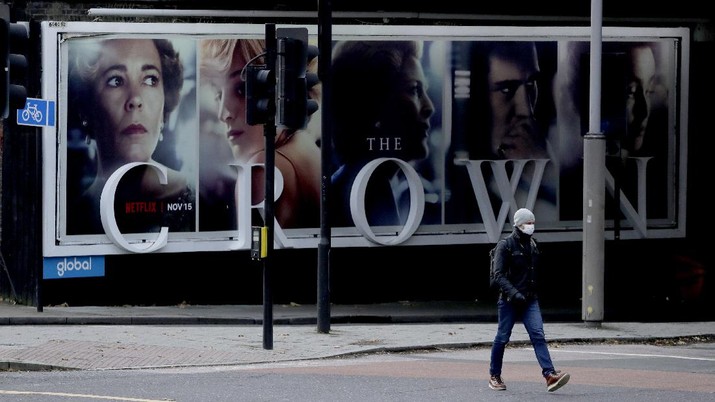 FILE - In this file photo dated Friday, Nov. 20, 2020, a man wearing a face mask walks past a billboard advertising 'The Crown' television series about Britain's Queen Elizabeth II and the royal family, during England's second coronavirus lockdown, in London.  Britain’s Culture Secretary Oliver Dowden in a newspaper interview published Sunday Nov. 29, 2020, said he thinks “The Crown” should come with a disclaimer as it’s a work of fiction with historical liberties taken in the Netflix drama about the British royal family. (AP Photo/Matt Dunham, FILE)