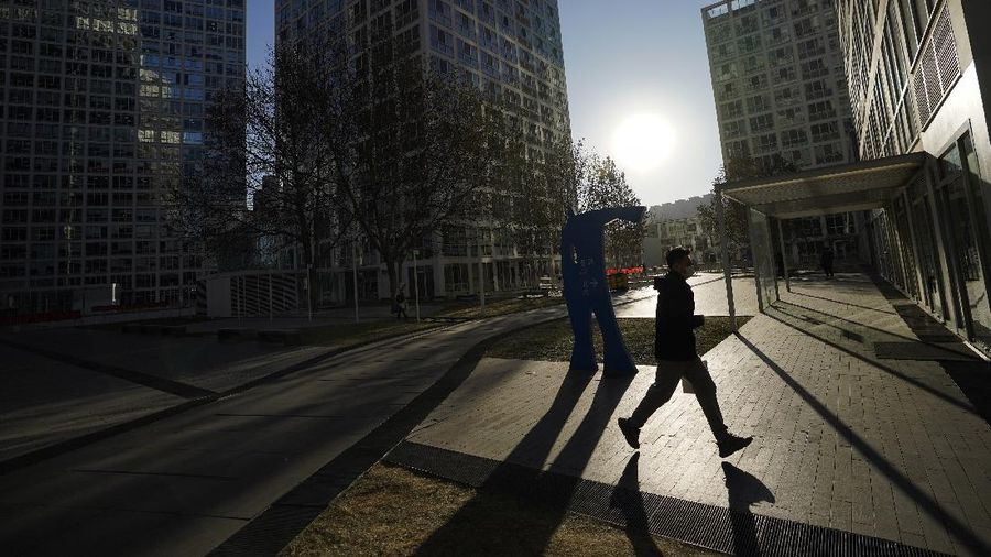 A man wearing a face mask to help curb the spread of the coronavirus runs past a commercial office buildings during the morning rush hour in Beijing, Monday, Jan. 4, 2021. Wary of another wave of infections, China is urging tens of millions of migrant workers to stay put during next month's Lunar New Year holiday, usually the world's largest annual human migration. (AP Photo/Andy Wong)