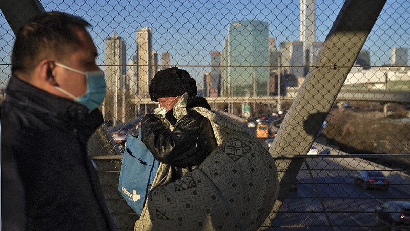 People wearing face masks to help curb the spread of the coronavirus walk on a pedestrian bridge against the Central Business District in Beijing, Tuesday, Jan. 5, 2021. Wary of another wave of infections, China is urging tens of millions of migrant workers to stay put during next month's Lunar New Year holiday, usually the world's largest annual human migration. (AP Photo/Andy Wong)