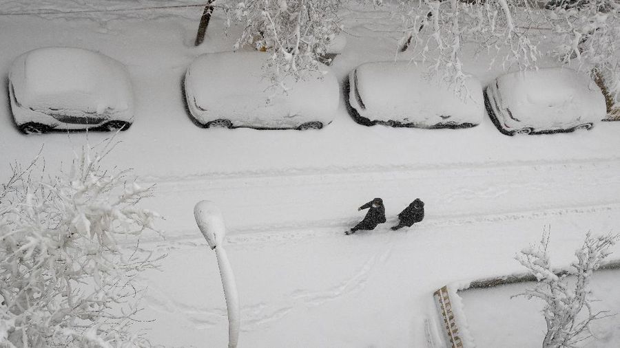 Two men walk slowly in the middle of a street after a heavy snowfall in Madrid, Spain, Saturday, Jan. 9, 2021. Spain is on high alert as a cold snap is covering much of the country with snow disrupting road, sea, rail and air traffic with the capital, Madrid enduring what the city's mayor described as 