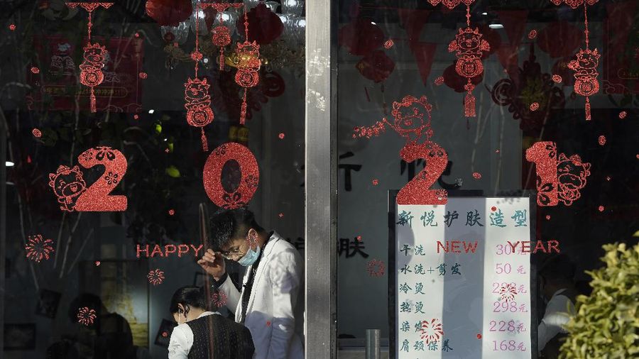 Employees stand near new year decorations at a beauty saloon in Beijing on Friday, Jan. 8, 2021. With next month's Lunar New Year travel rush looming, the government is telling people to stay put as much as possible and not travel to or from the capital Beijing. (AP Photo/Ng Han Guan)