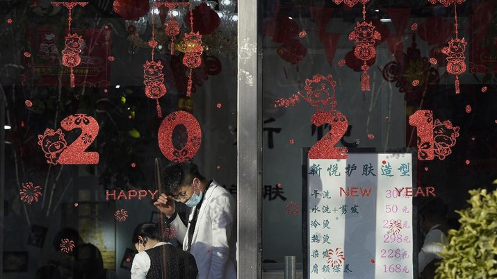 Employees stand near new year decorations at a beauty saloon in Beijing on Friday, Jan. 8, 2021. With next month's Lunar New Year travel rush looming, the government is telling people to stay put as much as possible and not travel to or from the capital Beijing. (AP Photo/Ng Han Guan)