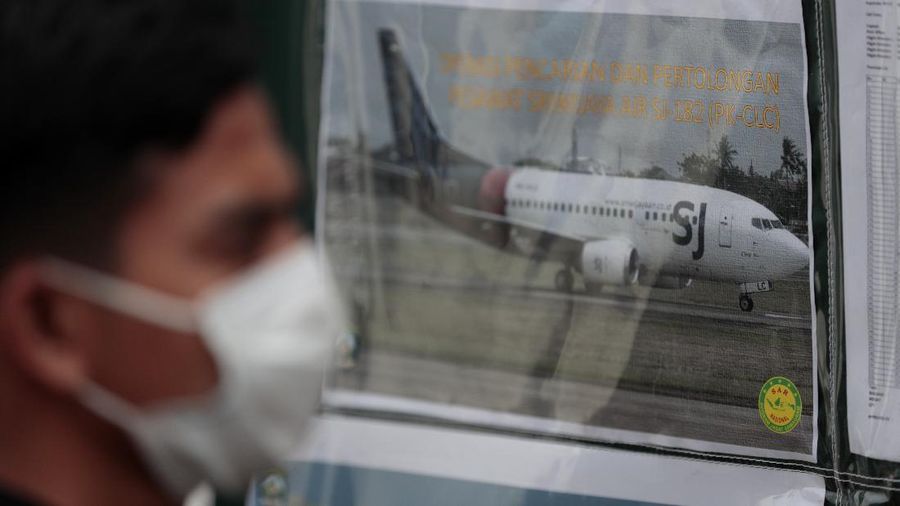 A man walks past a picture of Sriwijaya Air's passenger jet that crashed off Java island, put up at the command center for the search and rescue mission at Tanjung Priok Port in Jakarta, Indonesia, Sunday, Jan. 10, 2021. Indonesian rescuers pulled out body parts, pieces of clothing and scraps of metal from the Java Sea early Sunday morning, a day after a Boeing 737-500 with dozens of people onboard crashed shortly after takeoff from Jakarta, officials said. (AP Photo/Dita Alangkara)