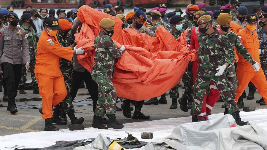 Tentara dan personel penyelamat menggunakan tenda terpal untuk membawa puing-puing yang ditemukan di perairan Pulau Jawa di sekitar tempat jet penumpang Sriwijaya Air jatuh, di Pelabuhan Tanjung Priok di Jakarta, Indonesia, Minggu, 10 Januari 2021.  (AP Photo/Tatan Syuflana)