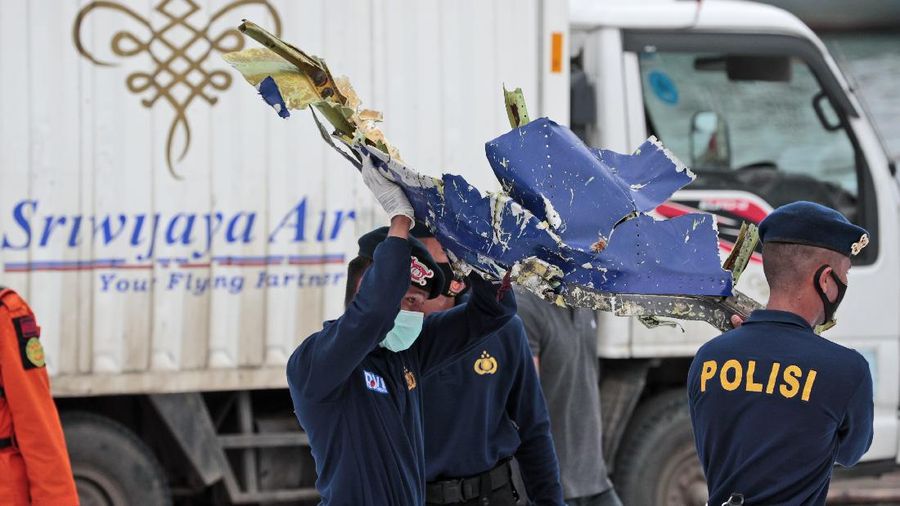 Police officers carry a part of aircraft recovered from Java Sea where a Sriwijaya Air passenger jet crashed, at Tanjung Priok Port in Jakarta, Indonesia, Monday, Jan. 11, 2021. The search for the black boxes of a crashed Sriwijaya Air jet intensified Monday to boost the investigation into what caused the plane carrying dozens of people to nosedive at high velocity into the Java Sea. (AP Photo/Dita Alangkara)