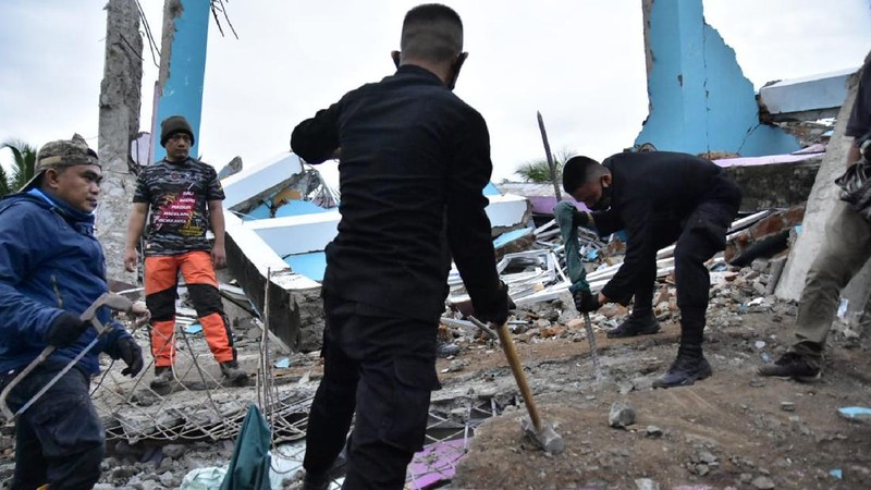 Recuers search for survivors among the ruin of a building damaged by an earthquake in Mamuju, West Sulawesi, Indonesia, Friday, Jan. 15, 2021. A strong, shallow earthquake shook Indonesia's Sulawesi island just after midnight, causing landslides and sending people fleeing from their homes in the nighttime darkness. (AP Photo/Sadly Ashari Said)