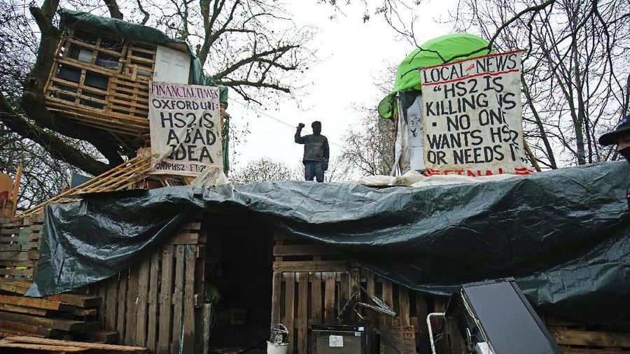 Para pengunjuk rasa duduk di atas pepohonan di perkemahan di Euston Square Gardens di pusat kota London, Inggris, Rabu (27/1/2021). (AP/Aaron Chown)