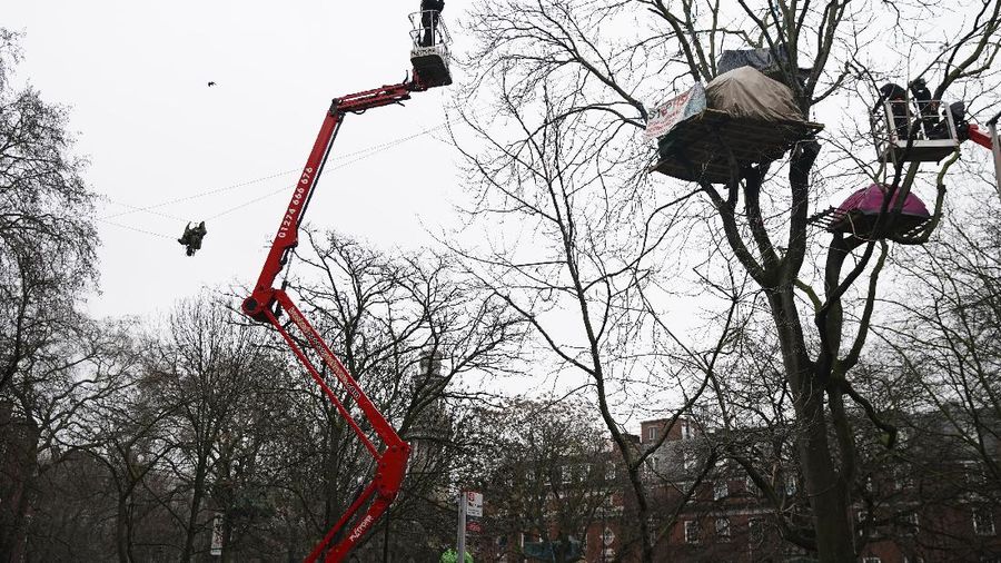 Para pengunjuk rasa duduk di atas pepohonan di perkemahan di Euston Square Gardens di pusat kota London, Inggris, Rabu (27/1/2021). (AP/Aaron Chown)
