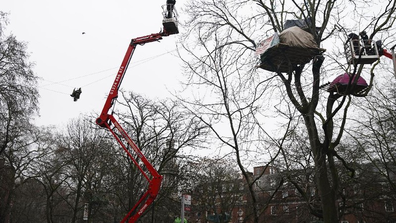 Para pengunjuk rasa duduk di atas pepohonan di perkemahan di Euston Square Gardens di pusat kota London, Inggris, Rabu (27/1/2021). (AP/Aaron Chown)