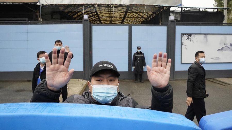 A security guard waves for journalists to clear the road after a convoy carrying the World Health Organization team entered the Huanan Seafood Market on the third day of a field visit in Wuhan in central China's Hubei province on Sunday, Jan. 31, 2021. Scientists initially suspected the coronavirus came from wild animals sold in the market. The market has since been largely ruled out but for the visiting WHO team of international researchers it could still provide hints to how the virus spread so widely. (AP Photo/Ng Han Guan)