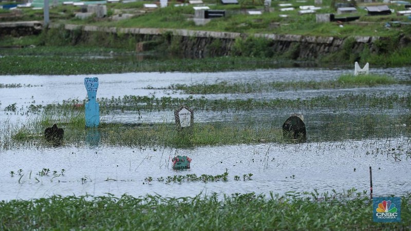 Warga melewati genangan air di pemakaman TPU Semper yang terendam banjir di Jakarta Utara, Rabu (3/2/2021). Banjir tersebut terjadi akibat tidak adanya saluran pembuangan air yang menyebabkan terendamnya ratusan makam. TPU Semper mengalami banjir sejak sekitar tahun 2000an akibat intensitas curah hujan yang tinggi. TPU Semper berada di atas lahan seluas sekitar 72 hektare dengan total 108.709 makam sejak dibuka pada 1984. Di bagian Selatan TPU adalah terminal peti kemas yang memanjang mengikuti luas area  (CNBC Indonesia/ Tri Susilo)