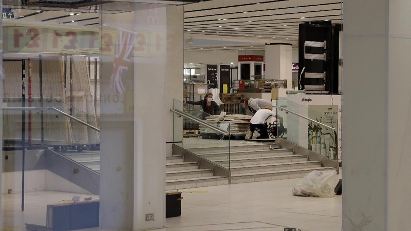A Union flag outside is reflected as workers are seen through entrance door windows packing items away inside the closed Debenhams flagship department store on Oxford Street in London, Saturday, Feb. 6, 2021, during England's third national lockdown since the coronavirus outbreak began. Online fashion firm Boohoo has bought the Debenhams brand and website for 55 million pounds ($75 million), in an acquisition which will see one of Britain's oldest department store chains turned into an online-only operation. The 118 stores will close for good as Boohoo sees little value in them when so much shopping now takes place online, a shift that has been accelerated by the coronavirus restrictions. (AP Photo/Matt Dunham)