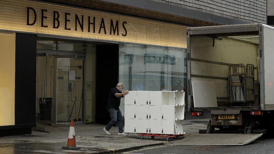 A Union flag outside is reflected as workers are seen through entrance door windows packing items away inside the closed Debenhams flagship department store on Oxford Street in London, Saturday, Feb. 6, 2021, during England's third national lockdown since the coronavirus outbreak began. Online fashion firm Boohoo has bought the Debenhams brand and website for 55 million pounds ($75 million), in an acquisition which will see one of Britain's oldest department store chains turned into an online-only operation. The 118 stores will close for good as Boohoo sees little value in them when so much shopping now takes place online, a shift that has been accelerated by the coronavirus restrictions. (AP Photo/Matt Dunham)