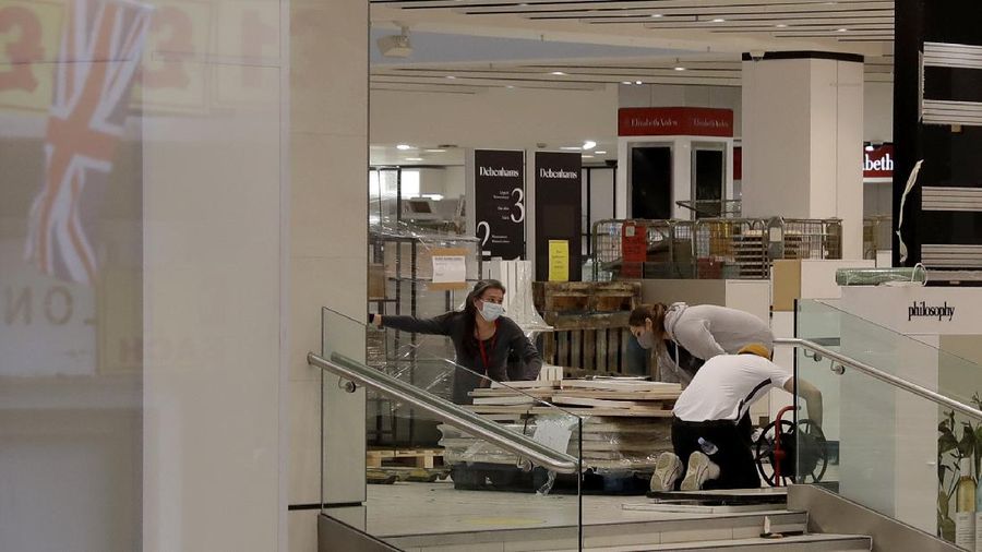 A Union flag outside is reflected as workers are seen through entrance door windows packing items away inside the closed Debenhams flagship department store on Oxford Street in London, Saturday, Feb. 6, 2021, during England's third national lockdown since the coronavirus outbreak began. Online fashion firm Boohoo has bought the Debenhams brand and website for 55 million pounds ($75 million), in an acquisition which will see one of Britain's oldest department store chains turned into an online-only operation. The 118 stores will close for good as Boohoo sees little value in them when so much shopping now takes place online, a shift that has been accelerated by the coronavirus restrictions. (AP Photo/Matt Dunham)