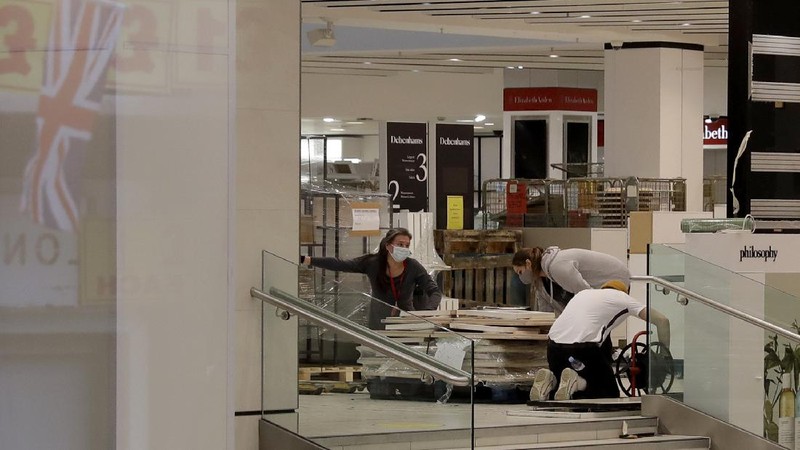 A Union flag outside is reflected as workers are seen through entrance door windows packing items away inside the closed Debenhams flagship department store on Oxford Street in London, Saturday, Feb. 6, 2021, during England's third national lockdown since the coronavirus outbreak began. Online fashion firm Boohoo has bought the Debenhams brand and website for 55 million pounds ($75 million), in an acquisition which will see one of Britain's oldest department store chains turned into an online-only operation. The 118 stores will close for good as Boohoo sees little value in them when so much shopping now takes place online, a shift that has been accelerated by the coronavirus restrictions. (AP Photo/Matt Dunham)