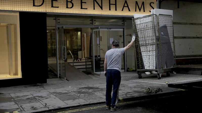A Union flag outside is reflected as workers are seen through entrance door windows packing items away inside the closed Debenhams flagship department store on Oxford Street in London, Saturday, Feb. 6, 2021, during England's third national lockdown since the coronavirus outbreak began. Online fashion firm Boohoo has bought the Debenhams brand and website for 55 million pounds ($75 million), in an acquisition which will see one of Britain's oldest department store chains turned into an online-only operation. The 118 stores will close for good as Boohoo sees little value in them when so much shopping now takes place online, a shift that has been accelerated by the coronavirus restrictions. (AP Photo/Matt Dunham)