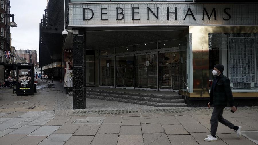 A Union flag outside is reflected as workers are seen through entrance door windows packing items away inside the closed Debenhams flagship department store on Oxford Street in London, Saturday, Feb. 6, 2021, during England's third national lockdown since the coronavirus outbreak began. Online fashion firm Boohoo has bought the Debenhams brand and website for 55 million pounds ($75 million), in an acquisition which will see one of Britain's oldest department store chains turned into an online-only operation. The 118 stores will close for good as Boohoo sees little value in them when so much shopping now takes place online, a shift that has been accelerated by the coronavirus restrictions. (AP Photo/Matt Dunham)