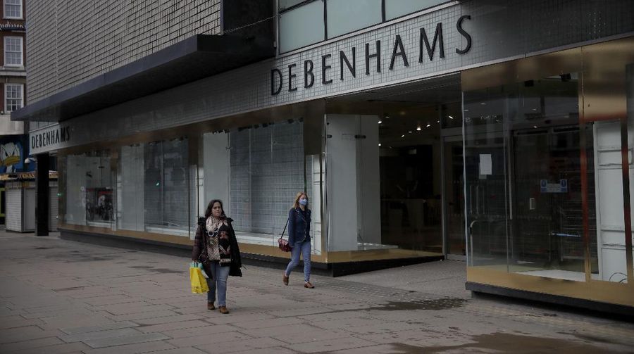 A Union flag outside is reflected as workers are seen through entrance door windows packing items away inside the closed Debenhams flagship department store on Oxford Street in London, Saturday, Feb. 6, 2021, during England's third national lockdown since the coronavirus outbreak began. Online fashion firm Boohoo has bought the Debenhams brand and website for 55 million pounds ($75 million), in an acquisition which will see one of Britain's oldest department store chains turned into an online-only operation. The 118 stores will close for good as Boohoo sees little value in them when so much shopping now takes place online, a shift that has been accelerated by the coronavirus restrictions. (AP Photo/Matt Dunham)