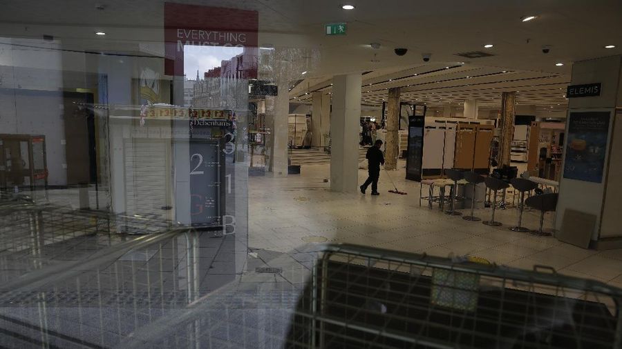 A Union flag outside is reflected as workers are seen through entrance door windows packing items away inside the closed Debenhams flagship department store on Oxford Street in London, Saturday, Feb. 6, 2021, during England's third national lockdown since the coronavirus outbreak began. Online fashion firm Boohoo has bought the Debenhams brand and website for 55 million pounds ($75 million), in an acquisition which will see one of Britain's oldest department store chains turned into an online-only operation. The 118 stores will close for good as Boohoo sees little value in them when so much shopping now takes place online, a shift that has been accelerated by the coronavirus restrictions. (AP Photo/Matt Dunham)