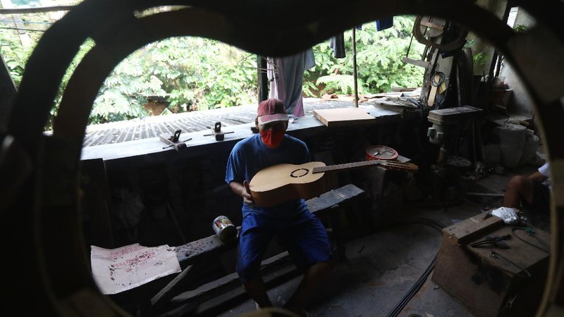 Pengrajjn  memperbaiki gitar pelanggan di servis gitar pak Manto, Jakarta Selatan, Senin (8/2/2021). Selain mereparasi gitar, Manto juga memproduksi gitar akustik yang dijual dari harga ratusan ribu hingga juta, tergantung jenis dan tingkat kesulitannya. (CNBC Indonesia/Andrean Kristianto)