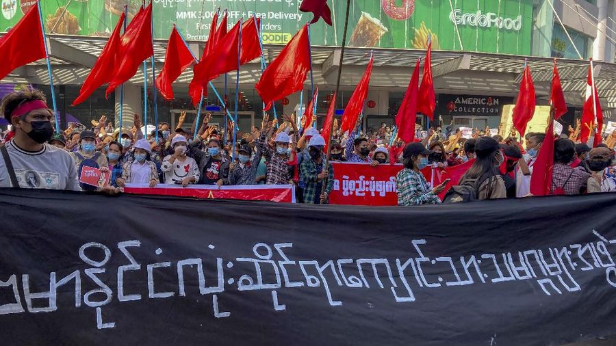 Campaigners with National League for Democracy party flags gather at an intersection in Yangon, Myanmar, Tuesday, Feb. 9, 2021. Protesters continued to gather Tuesday morning in Yangon breaching Myanmar's new military rulers ban of public gathering of five or more issued on Monday intended to crack down on peaceful public protests opposing their takeover. The banner reads:
