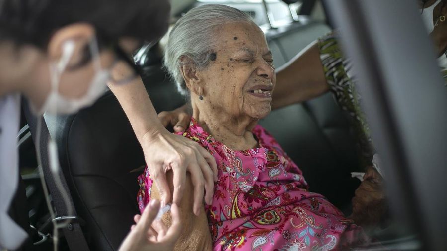 Maria de Lourdes, 101, grimaces as she receives a dose of the China's Sinovac Biotech COVID-19 vaccine at a drive-thru vaccination site in the Sambadrome, in Rio de Janeiro, Brazil, Saturday, Feb. 6, 2021. In a normal year, Rio’s Sambadrome would be preparing for its great moment of the year: the famous Carnival parade. But a week before what should be the start of Carnival, the pandemic has replaced pageantry. (AP Photo/Bruna Prado)