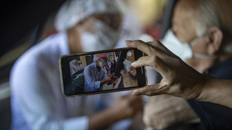 Health workers guide drivers to shots of China's Sinovac CoronaVac vaccine during a priority COVID-19 vaccination program for the elderly at a drive-thru set up in the Pacaembu soccer stadium parking lot in Sao Paulo, Brazil, Monday, Feb. 8, 2021. (AP Photo/Andre Penner)