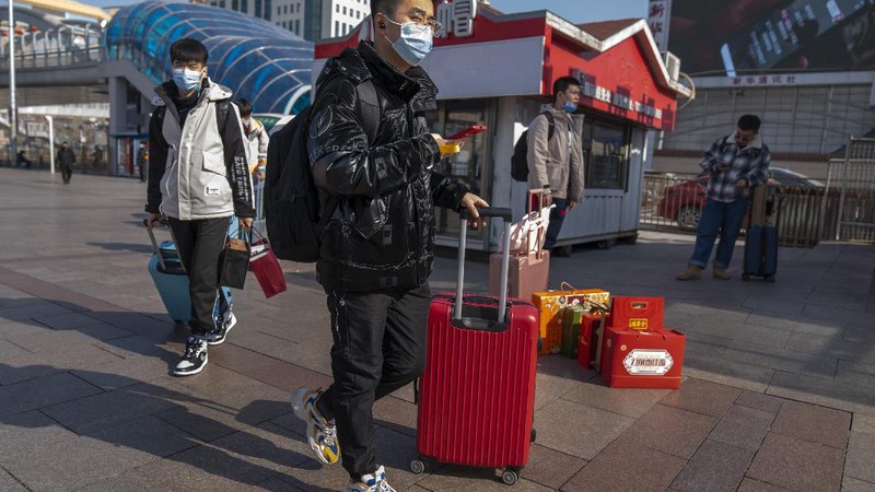 Travelers wearing face masks to protect against the coronavirus walk with their luggage outside the Beijing Railway Station in Beijing, Wednesday, Feb. 10, 2021. China appeared to be on pace for a slower than normal Lunar New Year travel rush this year after authorities discouraged people from traveling over the holiday to help maintain the nation's control over the ongoing COVID-19 pandemic. (AP Photo/Mark Schiefelbein)