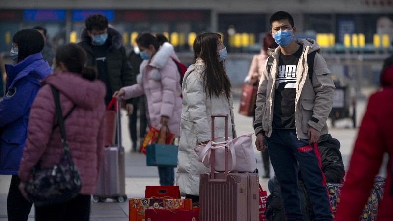 Travelers wearing face masks to protect against the coronavirus walk with their luggage outside the Beijing Railway Station in Beijing, Wednesday, Feb. 10, 2021. China appeared to be on pace for a slower than normal Lunar New Year travel rush this year after authorities discouraged people from traveling over the holiday to help maintain the nation's control over the ongoing COVID-19 pandemic. (AP Photo/Mark Schiefelbein)