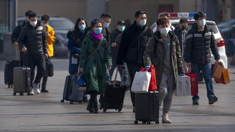Travelers wearing face masks to protect against the coronavirus walk with their luggage outside the Beijing Railway Station in Beijing, Wednesday, Feb. 10, 2021. China appeared to be on pace for a slower than normal Lunar New Year travel rush this year after authorities discouraged people from traveling over the holiday to help maintain the nation's control over the ongoing COVID-19 pandemic. (AP Photo/Mark Schiefelbein)