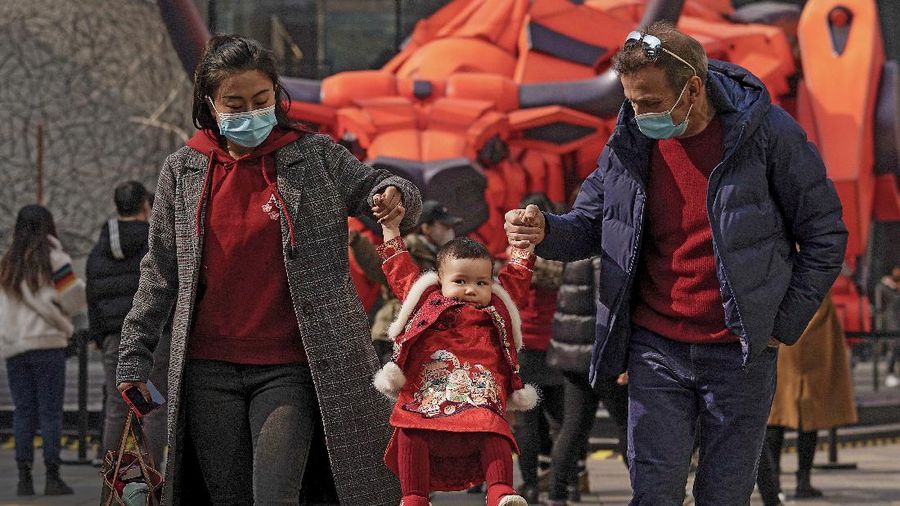 A couple wearing face masks to help curb the spread of the coronavirus lift their child wearing a new year costume as they visit to the capital city's popular shopping mall during the first day of the Lunar New Year in Beijing, Friday, Feb. 12, 2021. Festivities for the holiday, normally East Asia's busiest tourism season, are muted after China, Vietnam, Taiwan and other governments tightened travel curbs and urged the public to avoid big gatherings following renewed virus outbreaks. (AP Photo/Andy Wong)
