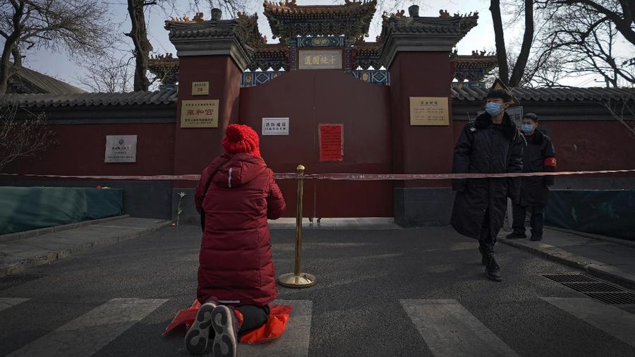 Security guards wearing face masks to help curb the spread of the coronavirus stand watch as a woman offers prayer near a barricade tape outside the closed Yonghegong Lama Temple, usually crowded with worshippers during the first day of the Lunar New Year in Beijing, Friday, Feb. 12, 2021. Festivities for the holiday, normally East Asia's busiest tourism season, are muted after China, Vietnam, Taiwan and other governments tightened travel curbs and urged the public to avoid big gatherings following renewed virus outbreaks. (AP Photo/Andy Wong)