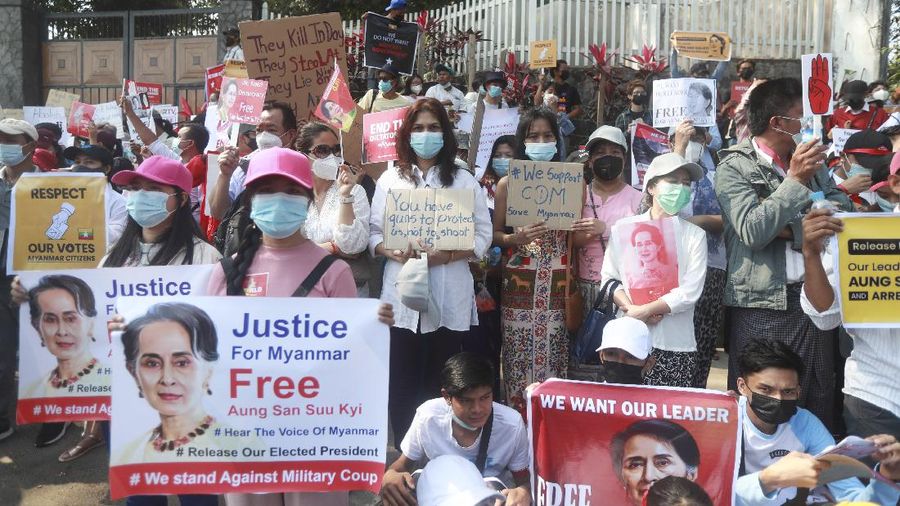 An anti-military coup protester flashes the three-fingered salute while other protesters hold placards that say 'We Don't Accept Military Coup' as they gather outside the Hledan Center in Yangon, Myanmar Saturday, Feb. 13, 2021. The daily protests in Myanmar's biggest city enters its second week despite a ban on public gatherings of five or more. (AP Photo)