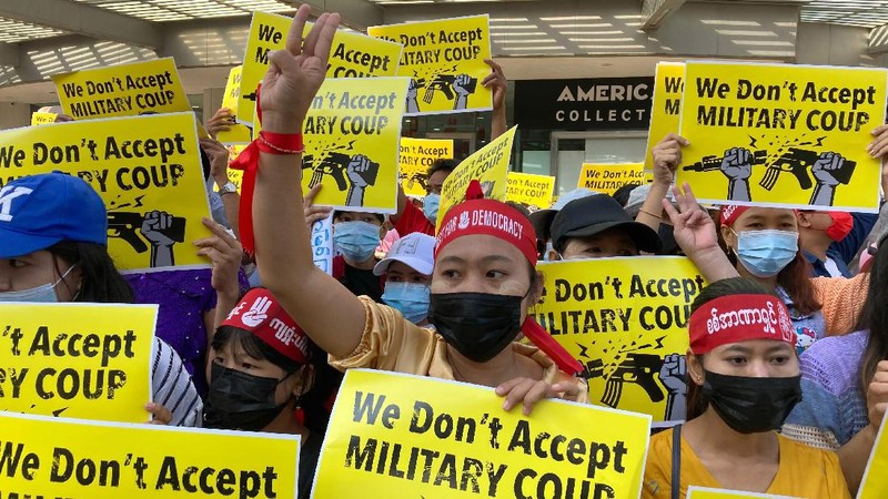 An anti-military coup protester flashes the three-fingered salute while other protesters hold placards that say 'We Don't Accept Military Coup' as they gather outside the Hledan Center in Yangon, Myanmar Saturday, Feb. 13, 2021. The daily protests in Myanmar's biggest city enters its second week despite a ban on public gatherings of five or more. (AP Photo)