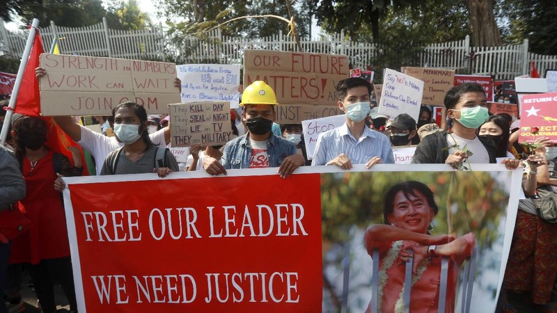 An anti-military coup protester flashes the three-fingered salute while other protesters hold placards that say 'We Don't Accept Military Coup' as they gather outside the Hledan Center in Yangon, Myanmar Saturday, Feb. 13, 2021. The daily protests in Myanmar's biggest city enters its second week despite a ban on public gatherings of five or more. (AP Photo)