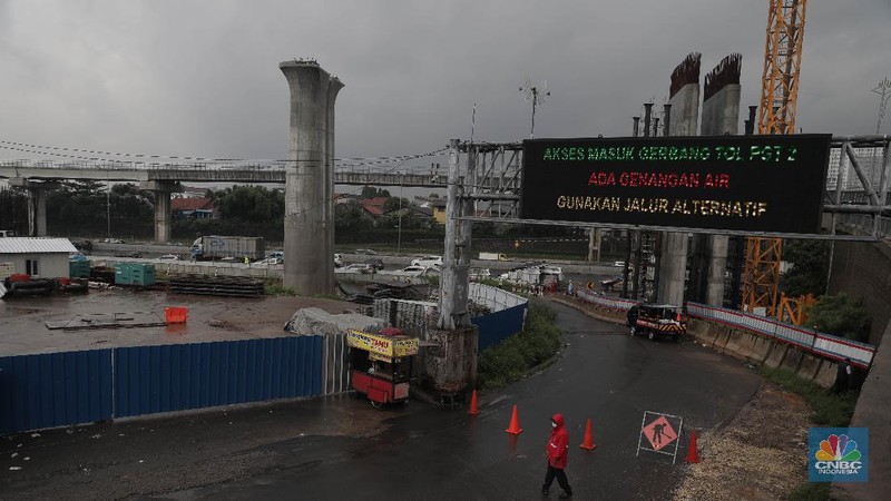 Petugas berjaga di bawah papan bertuliskan pengalihan arus karena genangan di Tol Jatibening, Jakarta, Jumat 19/2. Hujan semalaman yang mengguyur kawasan Jabodetabek membuat berbagai wilayah kebanjiran. Sejumlah kawasan tol pun terdampak banjir dan lumpuh. Akses masuk Gerbang Tol Jatibening arah Jakarta terpantau genangan. Tepatnya terjadi di lajur masuk Jatibening atau Cawang. Khusus kendaraan besar tetap dapat melintas, sementara kendaraan kecil golongan 1 dialihkan ke ruas Jalan Tol Dalam Kota. (CNBC Indonesia/ Muhammad Sabki)