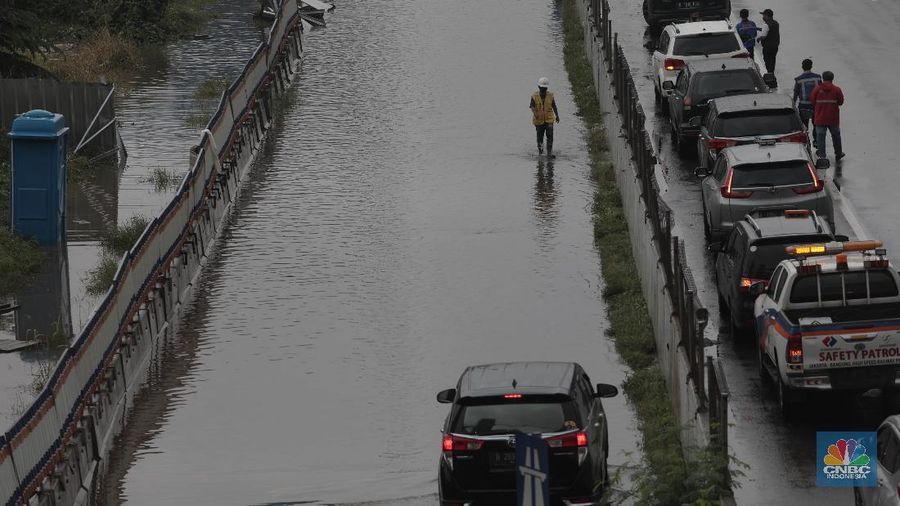 Petugas berjaga di bawah papan bertuliskan pengalihan arus karena genangan di Tol Jatibening, Jakarta, Jumat 19/2. Hujan semalaman yang mengguyur kawasan Jabodetabek membuat berbagai wilayah kebanjiran. Sejumlah kawasan tol pun terdampak banjir dan lumpuh. Akses masuk Gerbang Tol Jatibening arah Jakarta terpantau genangan. Tepatnya terjadi di lajur masuk Jatibening atau Cawang. Khusus kendaraan besar tetap dapat melintas, sementara kendaraan kecil golongan 1 dialihkan ke ruas Jalan Tol Dalam Kota. (CNBC Indonesia/ Muhammad Sabki)