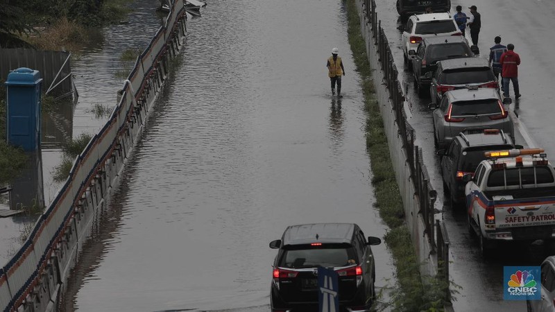Petugas berjaga di bawah papan bertuliskan pengalihan arus karena genangan di Tol Jatibening, Jakarta, Jumat 19/2. Hujan semalaman yang mengguyur kawasan Jabodetabek membuat berbagai wilayah kebanjiran. Sejumlah kawasan tol pun terdampak banjir dan lumpuh. Akses masuk Gerbang Tol Jatibening arah Jakarta terpantau genangan. Tepatnya terjadi di lajur masuk Jatibening atau Cawang. Khusus kendaraan besar tetap dapat melintas, sementara kendaraan kecil golongan 1 dialihkan ke ruas Jalan Tol Dalam Kota. (CNBC Indonesia/ Muhammad Sabki)
