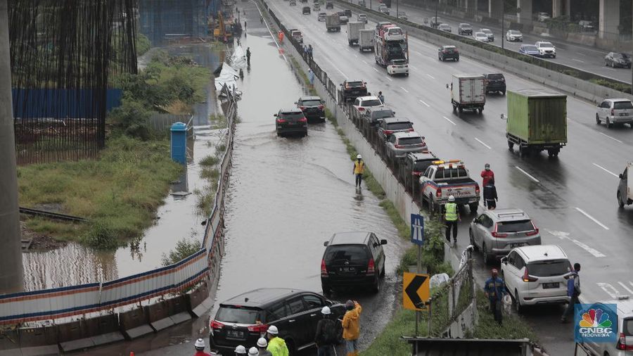 Petugas berjaga di bawah papan bertuliskan pengalihan arus karena genangan di Tol Jatibening, Jakarta, Jumat 19/2. Hujan semalaman yang mengguyur kawasan Jabodetabek membuat berbagai wilayah kebanjiran. Sejumlah kawasan tol pun terdampak banjir dan lumpuh. Akses masuk Gerbang Tol Jatibening arah Jakarta terpantau genangan. Tepatnya terjadi di lajur masuk Jatibening atau Cawang. Khusus kendaraan besar tetap dapat melintas, sementara kendaraan kecil golongan 1 dialihkan ke ruas Jalan Tol Dalam Kota. (CNBC Indonesia/ Muhammad Sabki)