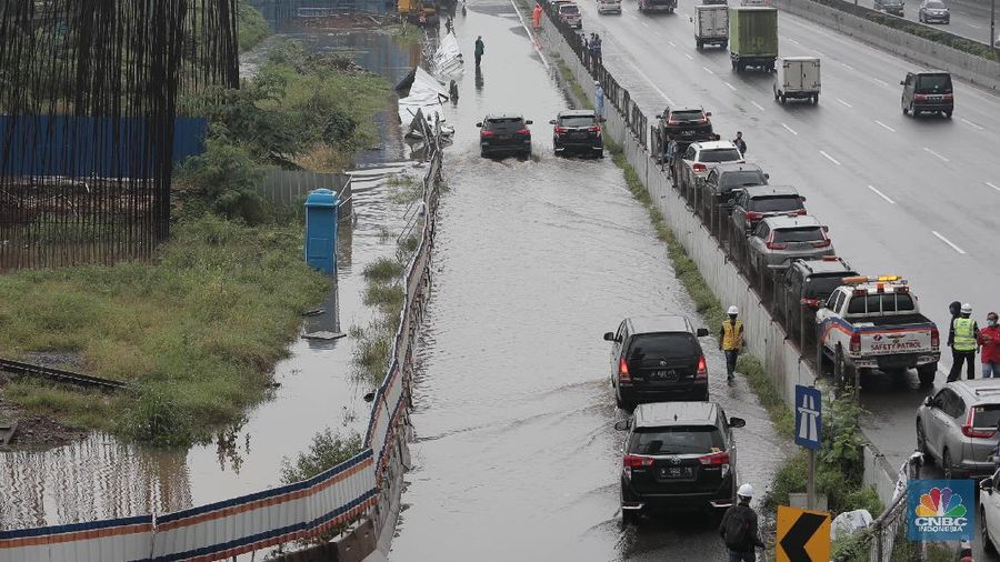 Petugas berjaga di bawah papan bertuliskan pengalihan arus karena genangan di Tol Jatibening, Jakarta, Jumat 19/2. Hujan semalaman yang mengguyur kawasan Jabodetabek membuat berbagai wilayah kebanjiran. Sejumlah kawasan tol pun terdampak banjir dan lumpuh. Akses masuk Gerbang Tol Jatibening arah Jakarta terpantau genangan. Tepatnya terjadi di lajur masuk Jatibening atau Cawang. Khusus kendaraan besar tetap dapat melintas, sementara kendaraan kecil golongan 1 dialihkan ke ruas Jalan Tol Dalam Kota. (CNBC Indonesia/ Muhammad Sabki)