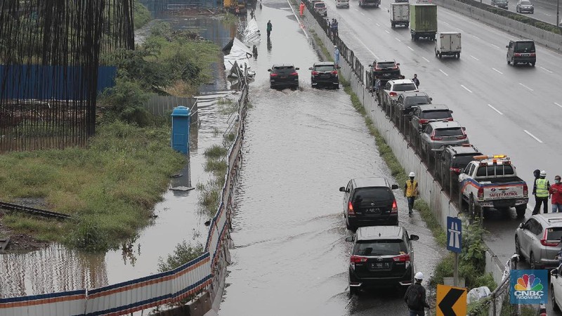 Petugas berjaga di bawah papan bertuliskan pengalihan arus karena genangan di Tol Jatibening, Jakarta, Jumat 19/2. Hujan semalaman yang mengguyur kawasan Jabodetabek membuat berbagai wilayah kebanjiran. Sejumlah kawasan tol pun terdampak banjir dan lumpuh. Akses masuk Gerbang Tol Jatibening arah Jakarta terpantau genangan. Tepatnya terjadi di lajur masuk Jatibening atau Cawang. Khusus kendaraan besar tetap dapat melintas, sementara kendaraan kecil golongan 1 dialihkan ke ruas Jalan Tol Dalam Kota. (CNBC Indonesia/ Muhammad Sabki)