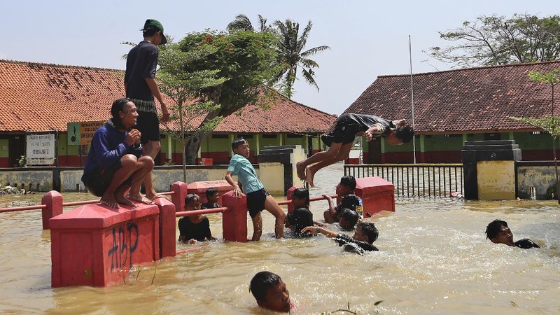 Indonesian youths play in the water during a flood in Bekasi, Indonesia, Monday, Feb. 22, 2021. Thousands of residents are being evacuated on the outskirts of Indonesia's capital amid flooding after the Citarum River embankment broke, officials said Monday. (AP Photo/Achmad Ibrahim)