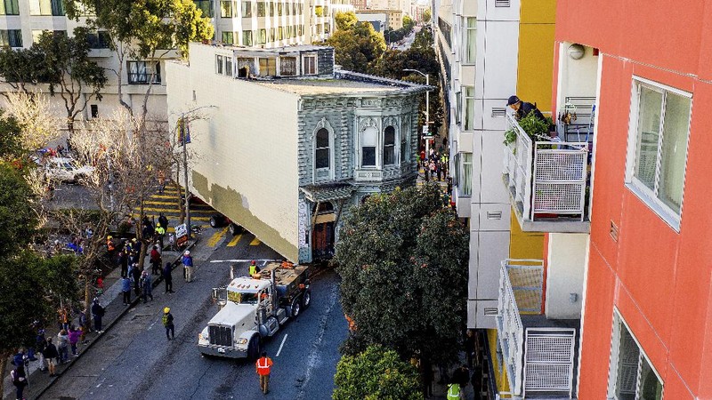 CORRECTS APPROXIMATE COST TO $400,000, INTEAD OF $200,000 - Crowds watch as a truck pulls a Victorian home through San Francisco on Sunday, Feb. 21, 2021. The house, built in 1882, was moved to a new location about six blocks away to make room for a condominium development. According to the consultant overseeing the project, the move cost approximately $400,000 and involved removing street lights, parking meters, and utility lines. (AP Photo/Noah Berger)