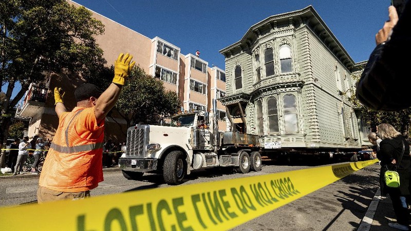 CORRECTS APPROXIMATE COST TO $400,000, INTEAD OF $200,000 - Crowds watch as a truck pulls a Victorian home through San Francisco on Sunday, Feb. 21, 2021. The house, built in 1882, was moved to a new location about six blocks away to make room for a condominium development. According to the consultant overseeing the project, the move cost approximately $400,000 and involved removing street lights, parking meters, and utility lines. (AP Photo/Noah Berger)